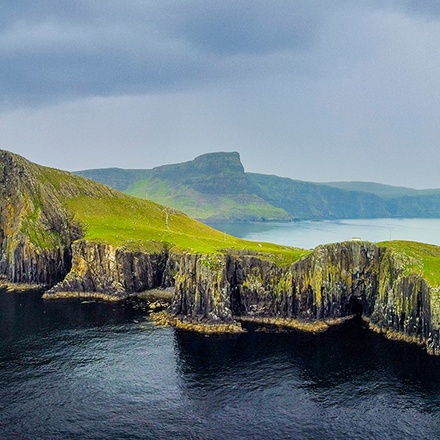 The Isle of Skye with a cliffside lighthouse visible under a stormy sky.
