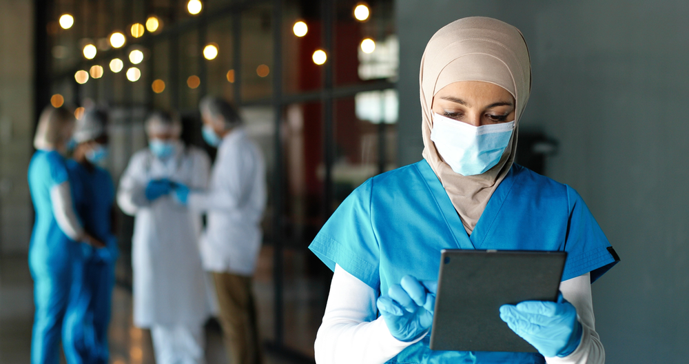 A healthcare worker in PPE interacts with a tablet.