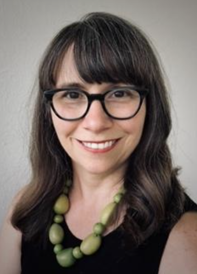 A person with a black shirt and large green beaded necklace is smiling at the camera.