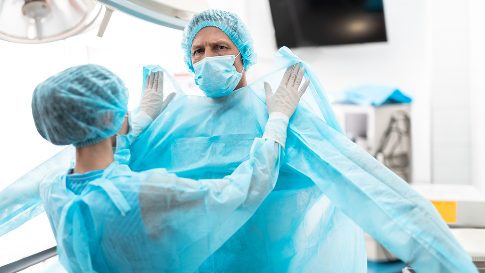 A surgeon dons a surgical gown.