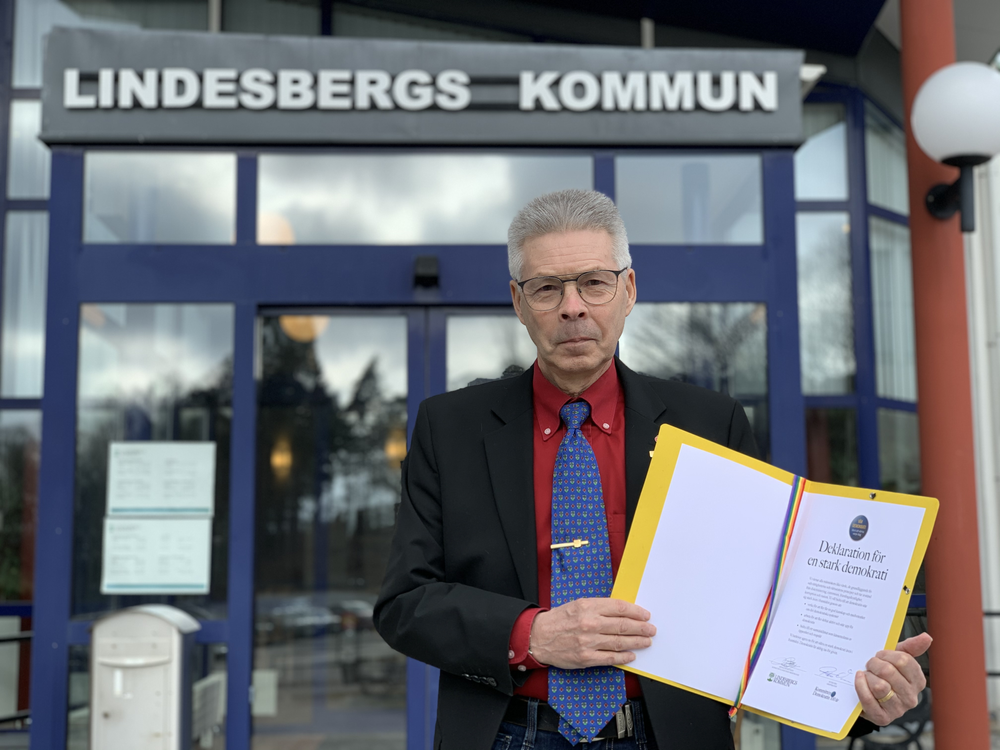 Kommunfullmäktiges ordförande Arnold Bengtsson står framför kommunhuset i Lindesberg med Deklarationen för stark demokrati i handen. 