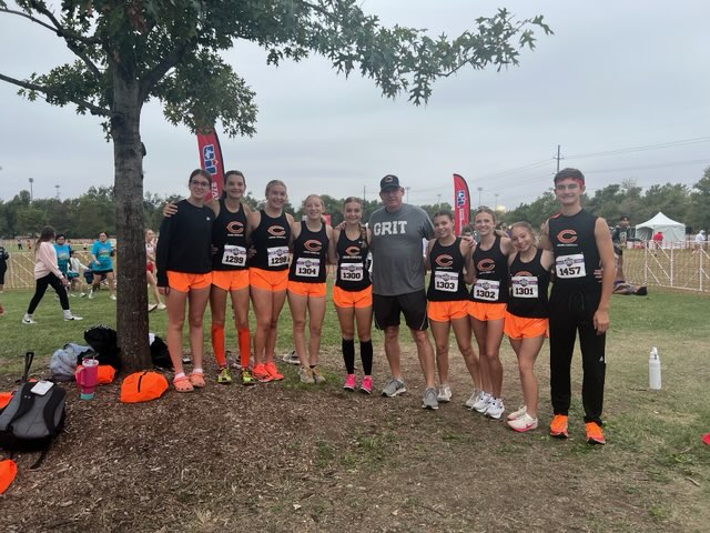 A group of young athletes pose with their coach after running their races.