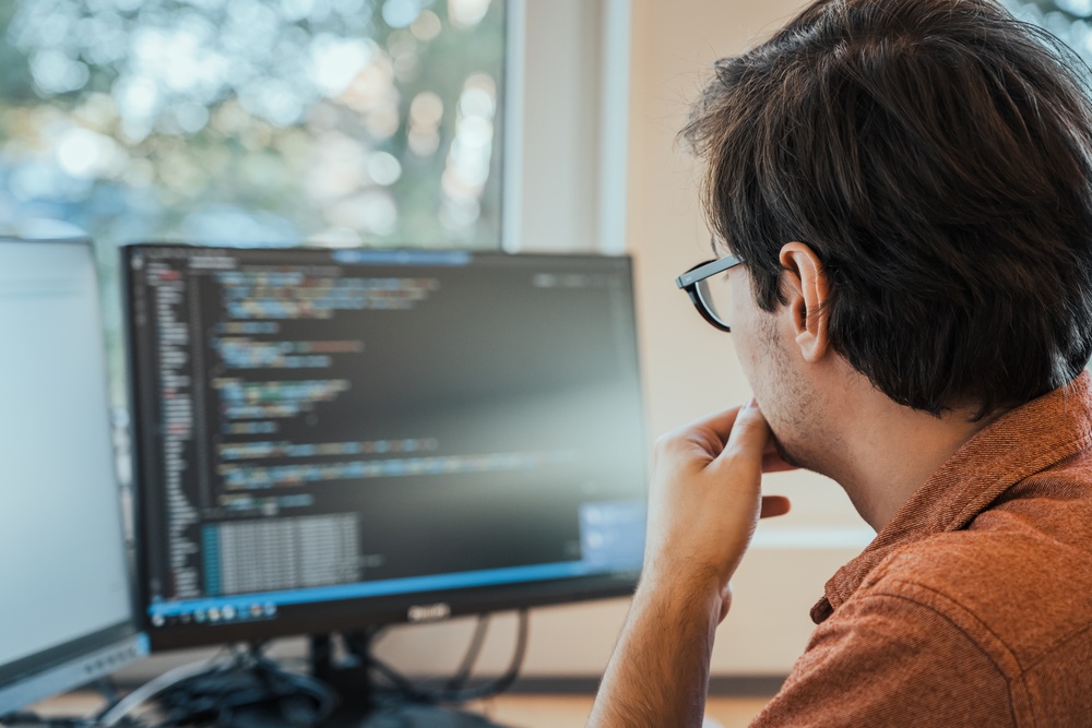 White young male in front of computer screen programming