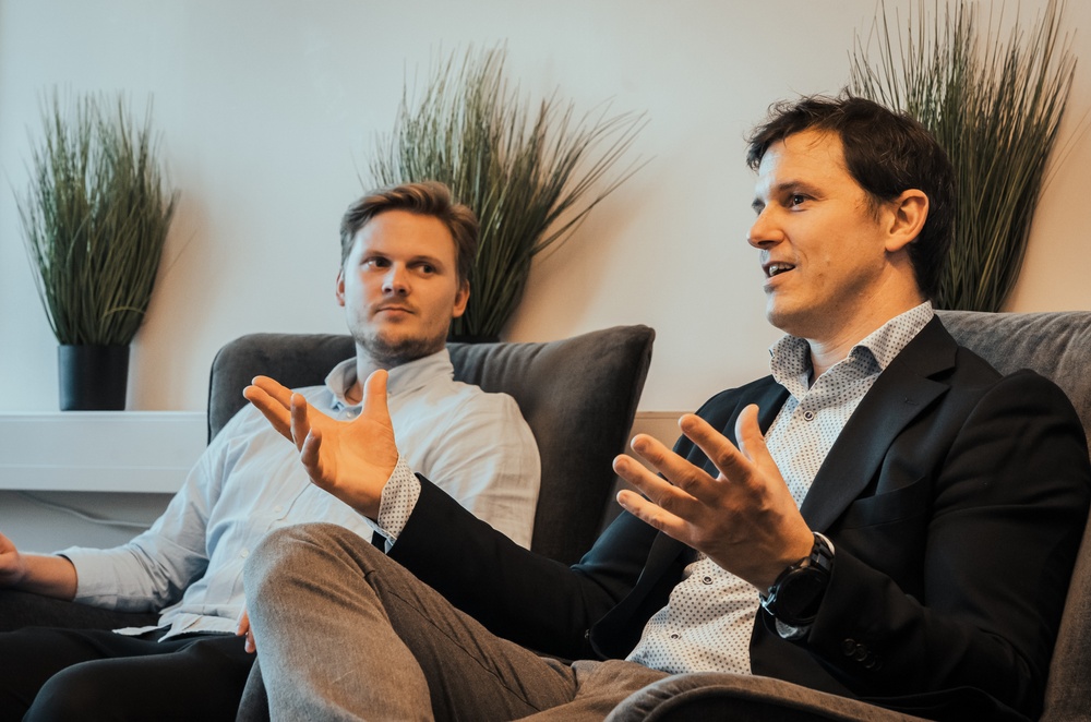 Two while men sitting in an office lounge area, discussing. 