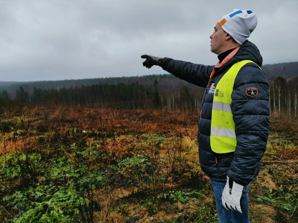 En man med vinterkläder står ute i naturen och pekar mot en markyta.