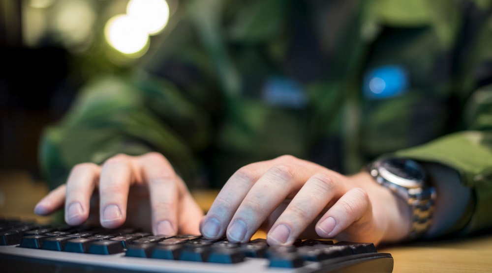 Person som skriver på ett tangentbord i kamouflagekläder.