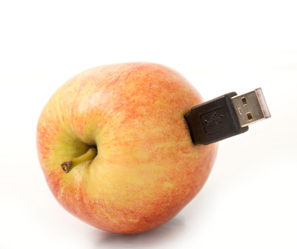 A white backbround and a red and yellow apple with a black USB memory stick sticking out of it.