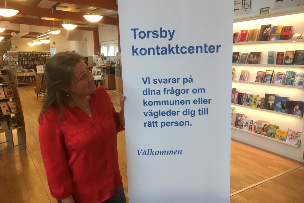 En kvinna står vid en roll up med texten Kontaktcenter, inomhus.