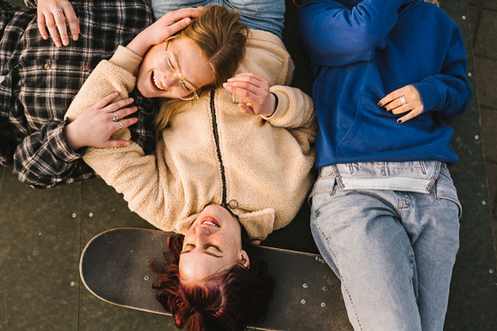 Tre ungdomat ligger på rygg och skrattar med en skateboard.