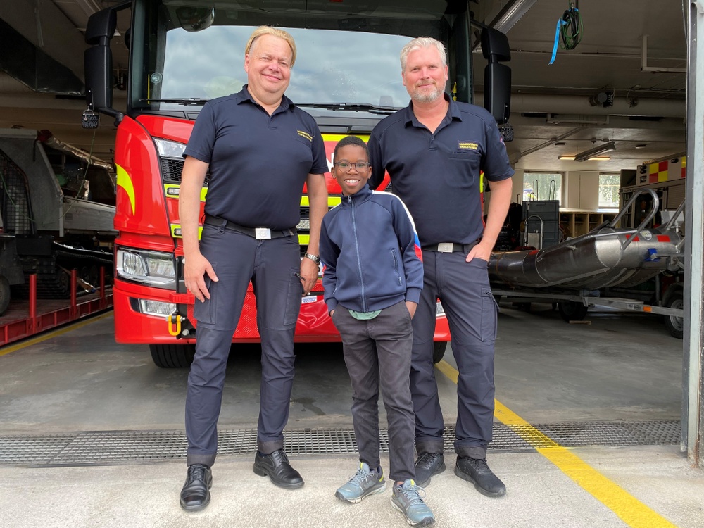 Joel Krantz, 10 år, på besök hos räddningstjänsten. Han står framför en brandbil och har Per Silverliden till vänster, förbundschef Medelpads räddningstjänstförbund, och insatsledare Magnus Rudberg till höger.