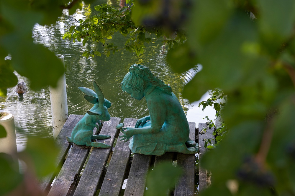 A bright green sculpture of a kneeling girl and a rabbit, seated next to a pond by artist Kim Simonsson.