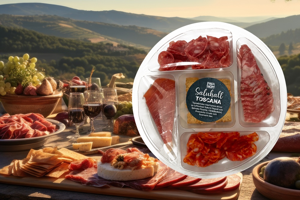 Uppdukat bord med toscaska delikatesser, i bakgrunden ser man ett böljande landskap. Bild på tapasbrickan Toscana fylld med lufttorkad  chark och kex.