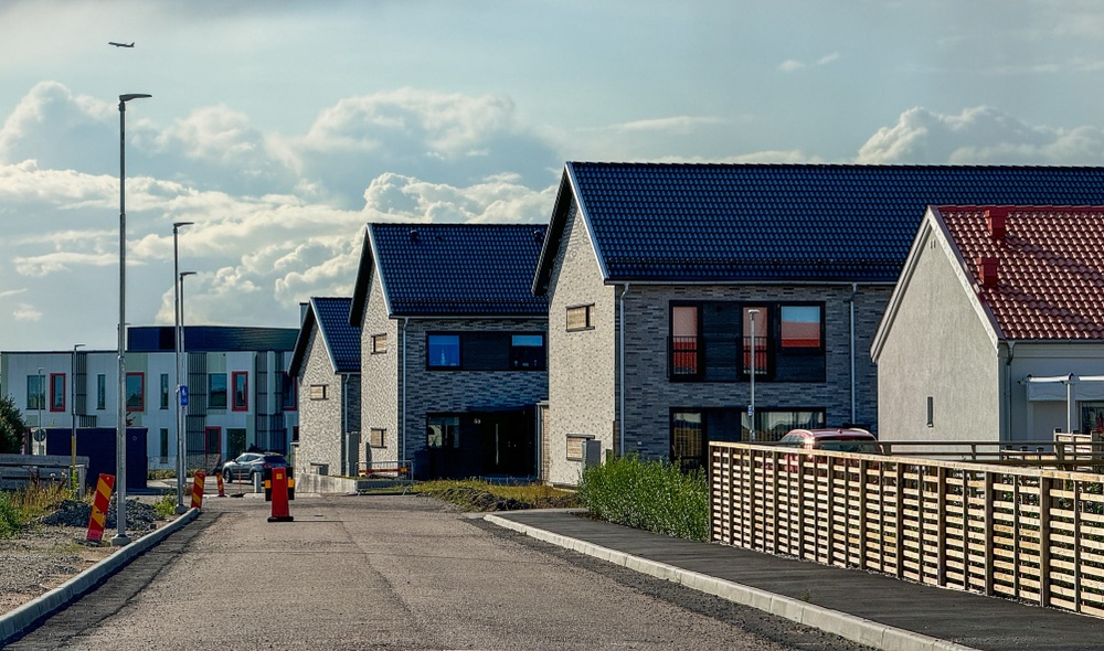 Gata med trästaket längs trottoaren, vitt hus och grå tvåvåningshus.