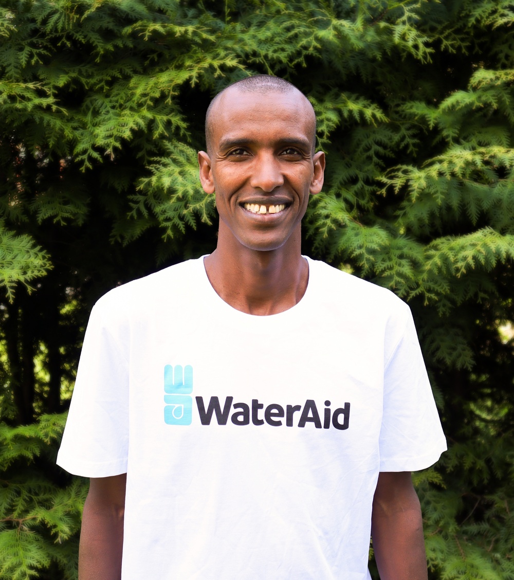 Bild på Mustafa Mohamed i tröja med WaterAids logga. Bilden är tagen utomhus framför grön buske.