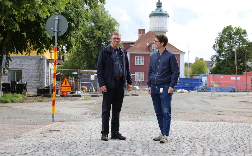 Två personer står på en gata framför en byggplats.