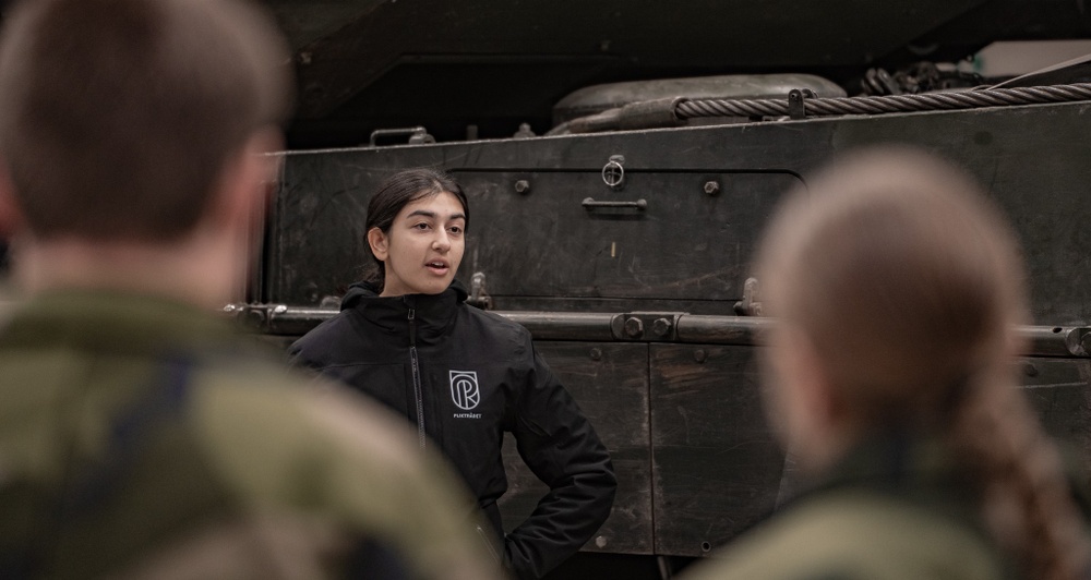 Kvinna som talar med soldater framför en stridsvagn. 