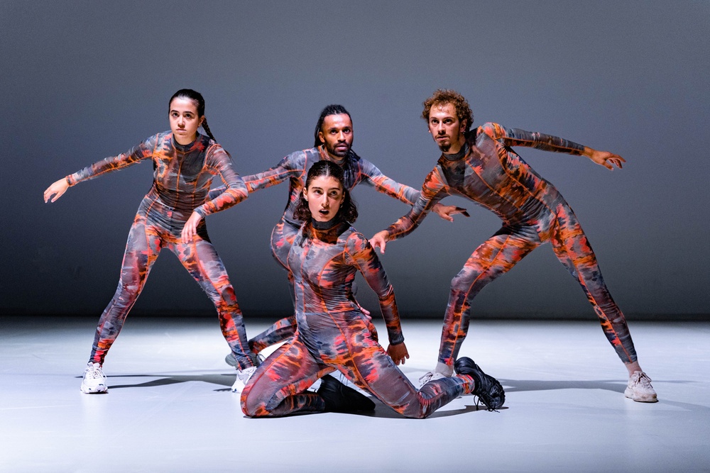 Fyra dansare i grå-orange kropsstrumpor tittar in i kameran.