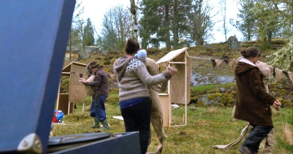 Tre personer dansar med dockor utomhus.