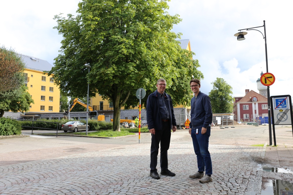 Två personer står på en gata framför en byggplats.