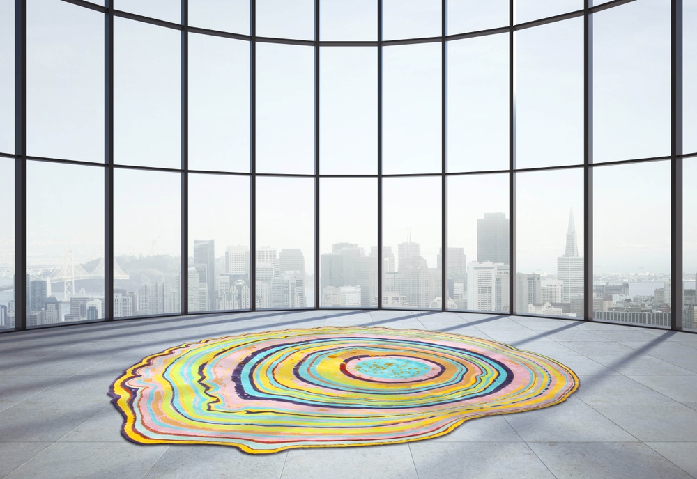 A tufted wool rug with a motif of swirls of vivid colours stemming from an epicenter with pink as the dominating colour and covering the entire surface of the rug, resembling an agate stone.