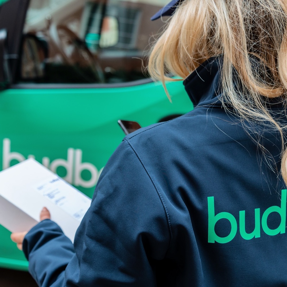 Picture of a Budbee driver holding a parcel with a Budbee green vehicle in the background 