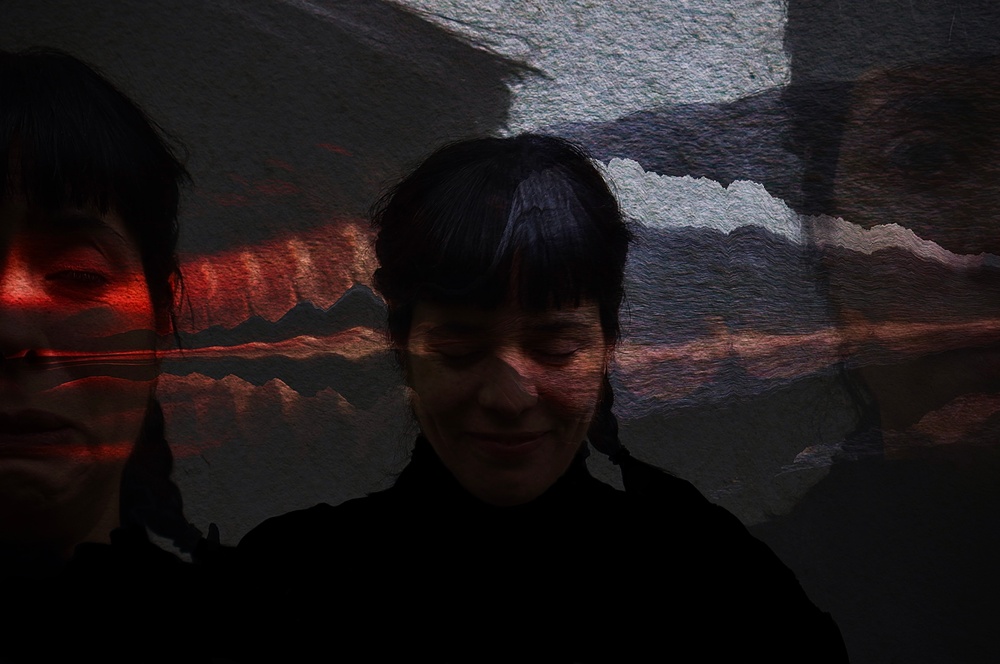 I bakgrunden syns ett porträtt av Mari Carrasco. Svarta skuggor ligger över bilden.