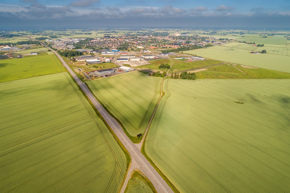 Drönarbild över område med åkermark i förgrunden och ett samhälle i bakgrunden.