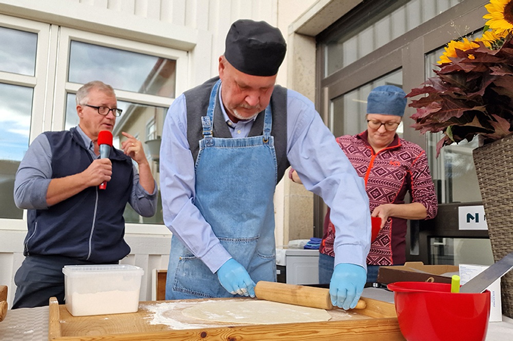 Två män och en kvinna. Mannen i mitten kavlar ut en bulldeg.