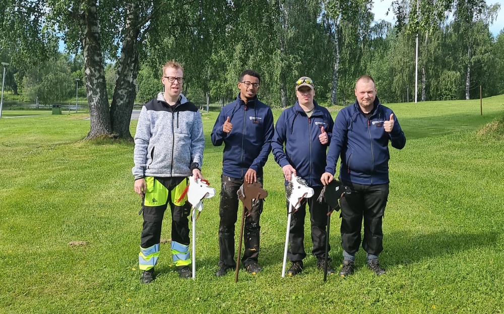 Fyra män står med käpphästar i grönskande park.