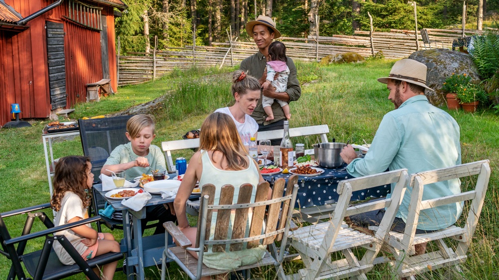 Familj sitter vid trädgårdsbord och äter. 