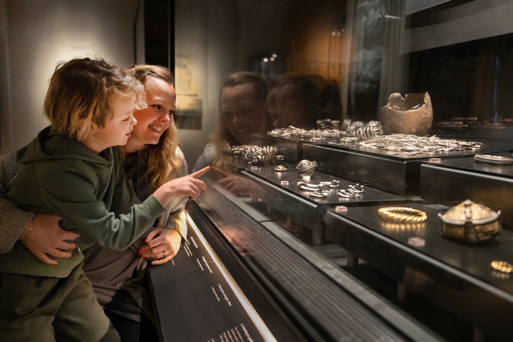 En mamma och hennes son. De tittar på en museimonter med silverskatter. 