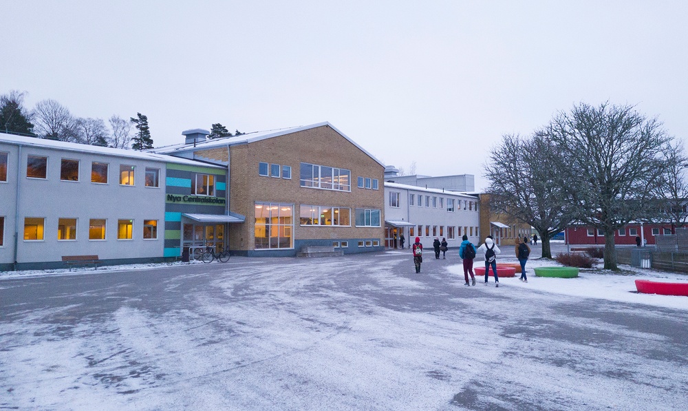 Nya Centralskolans skolgård i förgrunden, skolan i bakgrunden. Lite snö på marken. Några elever går mot skolan. 