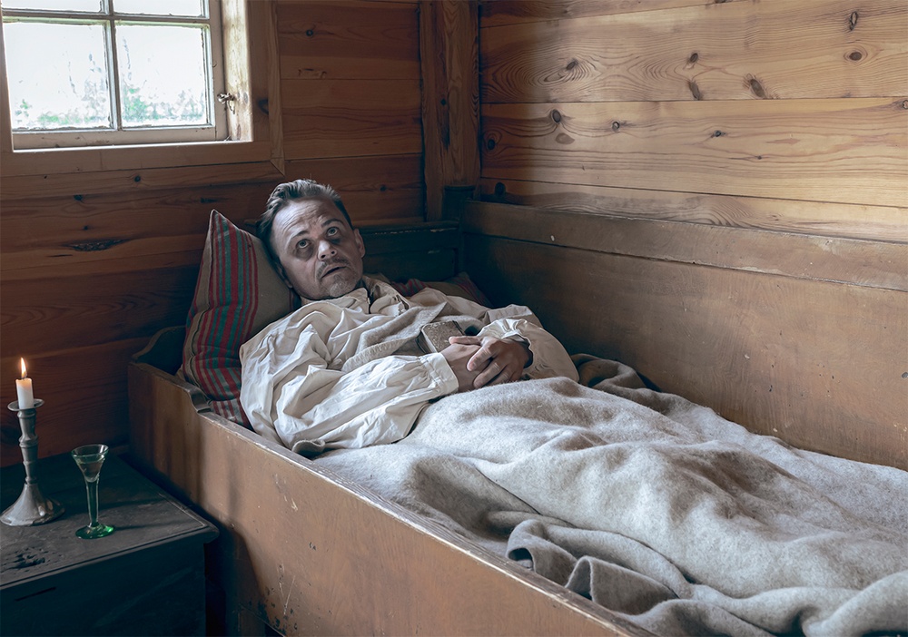 En svårt sjuk man som ligger i nerbäddad i en säng. Drabbad av pesten. 