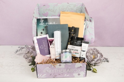 A My Thera Box subscription box filled with a candle, skin cream, fragrances, a notebook and other self care goodies.