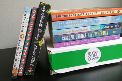 A closed Book of the Draw subscription box with several books on top of it and leaning against it.