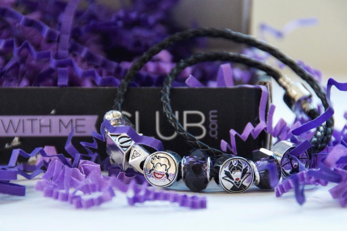 A Charm With Me Club subscription box filled with purple crinkle paper and a bracelet with several charms on it.