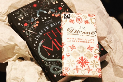 A book nestled in tissue paper with a bar of white chocolate on top of it, from a Chocolate and Book subscription box.