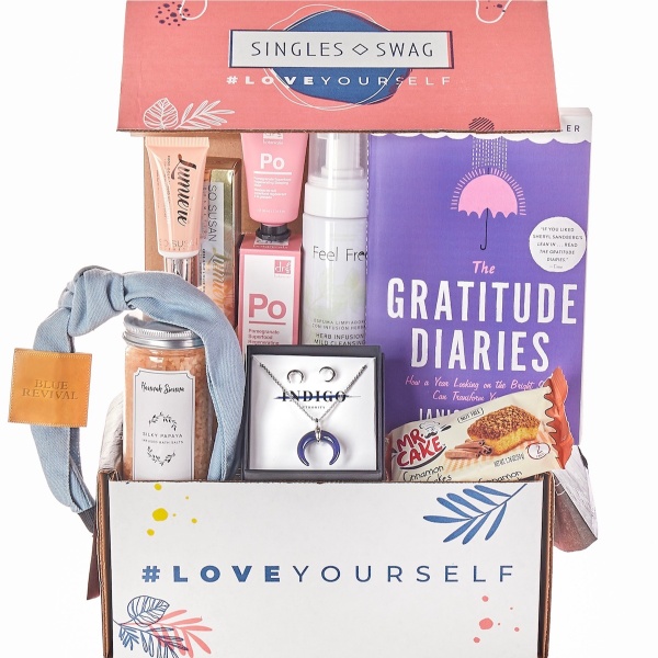 A SinglesSwag subscription box filled with a book, snacks, jewelry and makeup.