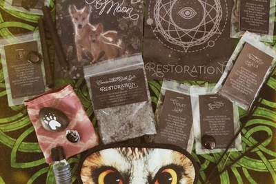 Items from an Antipodean Witch subscription box, including packets of herbs, a ring, stones, a sleep mask and candles.