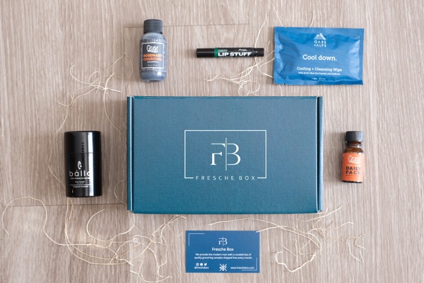A closed, blue Freshe subscription box surrounded by quality grooming samples for men.
