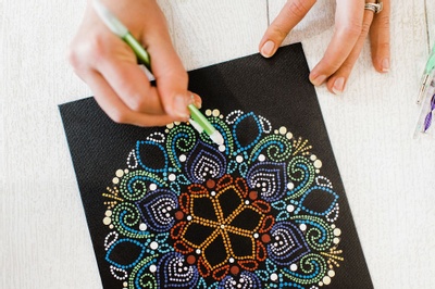 A person drawing a colorful mandala on black paper.
