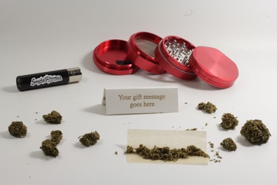 Items from a Stoner Bundle subscription box, including a little paper that says your gift message goes here and marijuana.