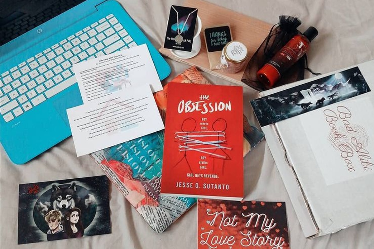 Items from a Bad Alibi Book subscription box, including a murder mystery book, lotion, note cards and more.