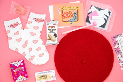 A love-themed subscription box. Items include  socks, conversation heart candies, a funny greeting card, enamel pin, and a french beret.