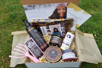 A white and gold box filled with items for curly hair including super sweetback treatment, hair oil, a comb and more.