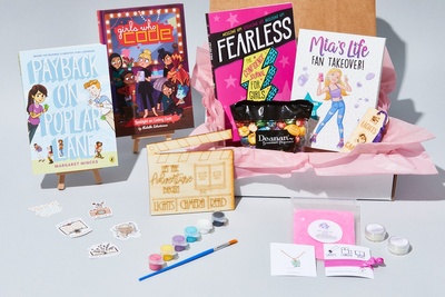 An open Between the Bookends subscription box filled with books for tweens, paints and jewelry.