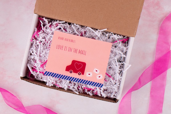An open Bombs and Bubbles subscription box with a card inside it that says Love is in the mail.