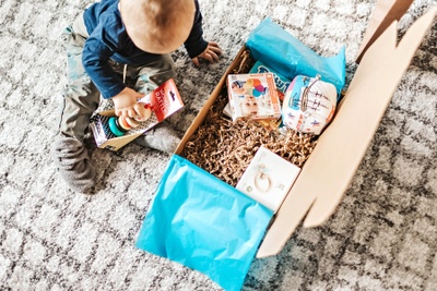 Seen from above, a baby boy sitting in front of a Hoppi subscription box and playing with baby toys from the box.