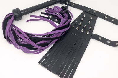 Items from a Kink Crate subscription box, including a black and purple whip and a metal studded belt.