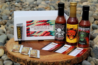 A subscription box that says Hot Sauce of the Month Club, which contains 3 types of hot sauce and a curry paste.